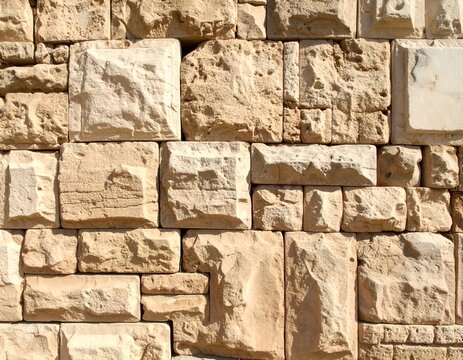 Close-up of a textured sandstone wall, varying shapes and hues of tan and cream