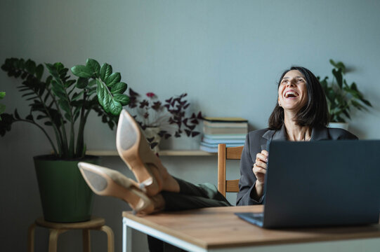 Happy businesswoman relaxes with feet on desk at home office
