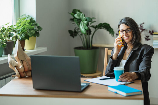 Smiling businesswoman talks on smartphone at office desk