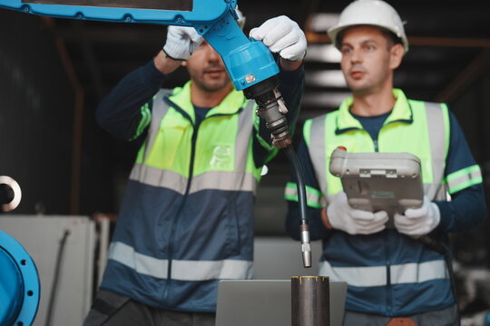 Industrial workers operating robotic arm and using tablet in manufacturing facility
