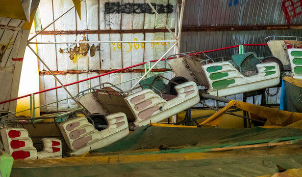 View of abandoned amusement park ride cars with worn paint and metal frames inside a derelict structure in Elektrenai, Vilnius County, Lithuania.
