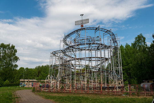 View of an abandoned roller coaster structure in an overgrown park with trees and a blue sky in Elektrenai, Vilnius County, Lithuania.