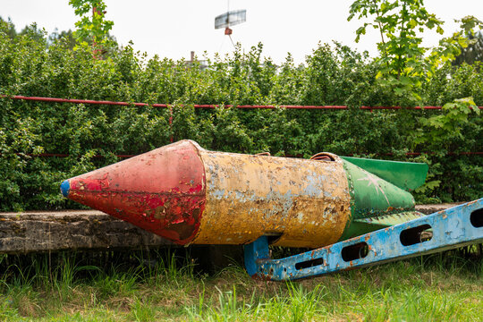 View of a weathered, vintage rocket-shaped playground ride with peeling paint, situated in a park with green bushes in the background in Elektrenai, Vilnius County, Lithuania.