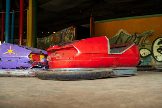 View of abandoned red and purple bumper cars in a derelict amusement park with graffiti-covered walls in Elektrenai, Vilnius County, Lithuania.