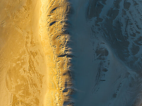 Aerial view of Nanarup Sand dunes showing the contrast between sunlit golden sand and deep blue shadows in the landscape of Albany, WA, Australia.