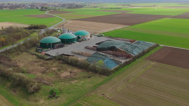 Aerial view of biogas plant with green dome-shaped digesters and storage areas surrounded by agricultural fields in Gross-Umstadt, Hessen, Germany.