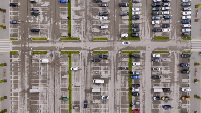 Aerial view of a large parking lot with numerous cars parked in organized rows on asphalt with green grass dividers in Riga, Latvia.