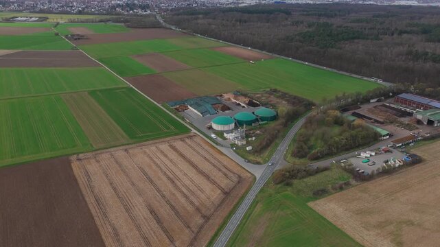 Aerial view of a biogas plant with green circular digesters surrounded by agricultural fields and a road in Gross-Umstadt, Hessen, Germany.