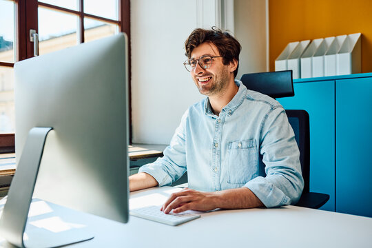 Cheerful man uses computer at office desk