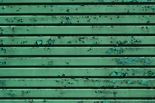 Peeling green paint on weathered ribbed metal surface with distressed texture and horizontal pattern