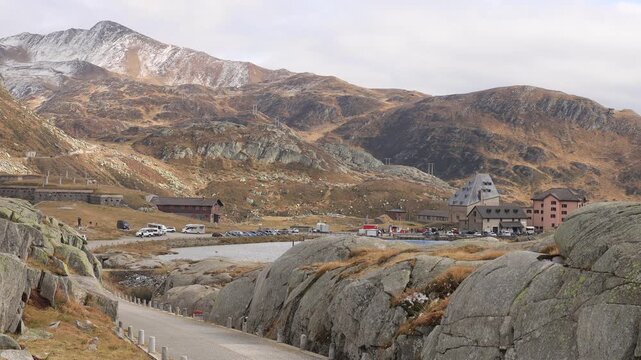 Gotthard Pass summit with hospice buildings, Airolo, Switzerland. Static shot of the alpine lake, parking area and snow dusted peaks in the Swiss Alps in autumn, a historic mountain pass