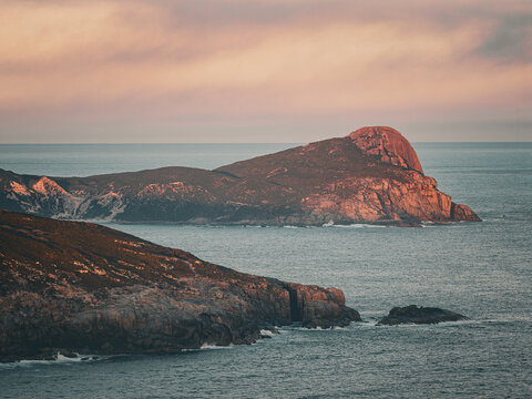 Aerial view of the rugged coastline of Torndirrup National Park with dramatic rocky cliffs and ocean waves at sunset in Torndirrup, Western Australia, Australia.