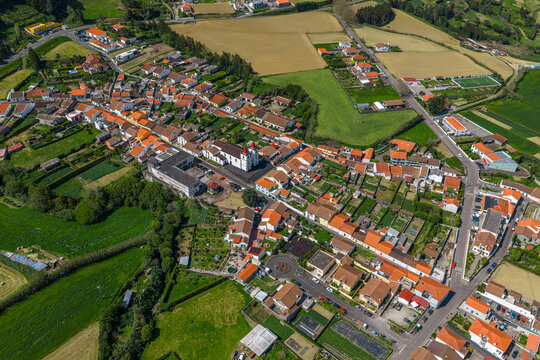 Aerial view of a village with red-tiled roofs and a central church surrounded by green agricultural fields and pastures in Maia, Acores, Portugal.
