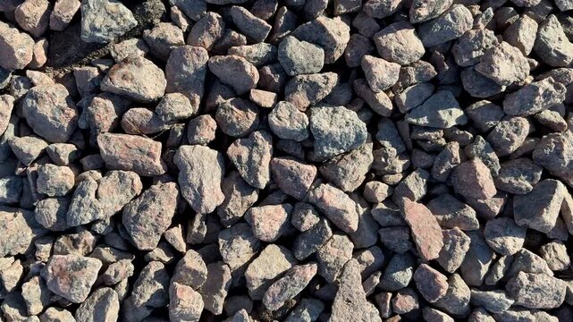 Closeup small gravel stones texture, sunlit rough pebbles in muted brown and gray tones, scattered angular fragments forming dense