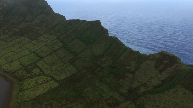 Aerial view of the Caldeirao volcanic crater with lush green fields and stone walls overlooking the Atlantic Ocean in Vila do Corvo, Acores, Portugal.