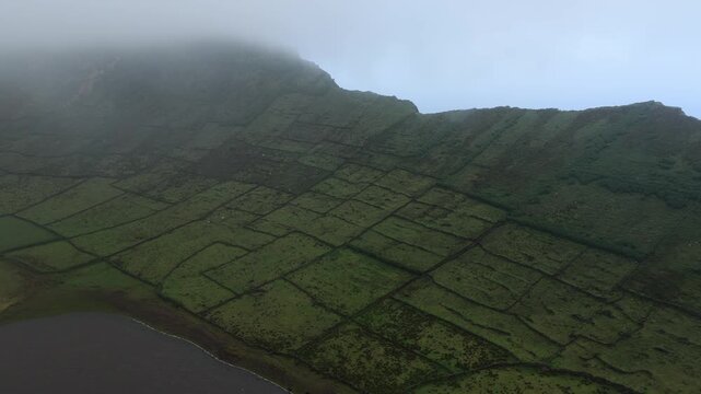 Aerial view of Caldeirao crater featuring ancient stone walls dividing lush green fields on the volcanic landscape of Vila do Corvo, Acores, Portugal.