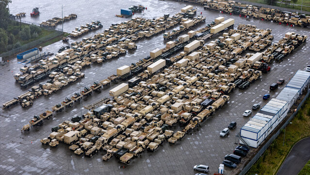 Aerial view of a large parking lot filled with numerous military trucks, trailers, and shipping containers parked in organized rows in Gdansk, Pomeranian Voivodeship, Poland.