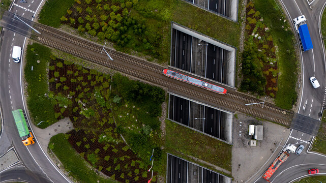 Aerial view of a train crossing a bridge over a highway intersection surrounded by green spaces and roads in Gdansk, Pomeranian Voivodeship, Poland.