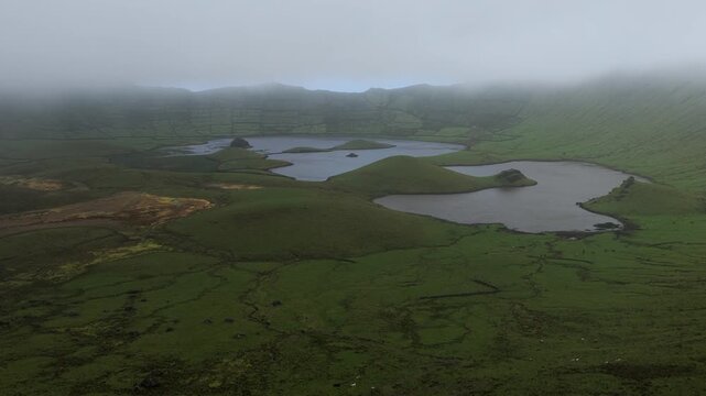 Aerial view of the volcanic Caldeirao crater lake with green hills and mist in Vila do Corvo, Acores, Portugal.