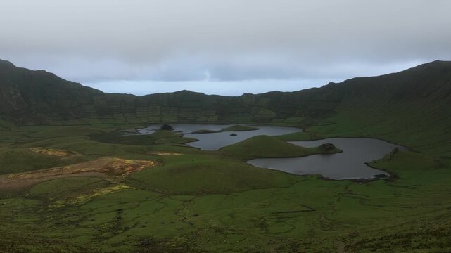 Aerial view of the lush green Caldeirao volcanic crater lake surrounded by rolling hills and dramatic landscape in Vila do Corvo, Acores, Portugal.