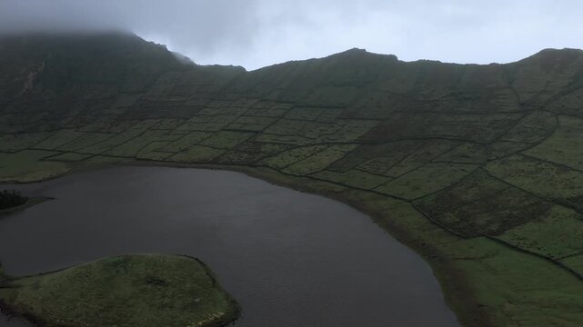 Aerial view of the Caldeirao volcanic crater lake surrounded by lush green fields and stone walls in Vila do Corvo, Acores, Portugal.