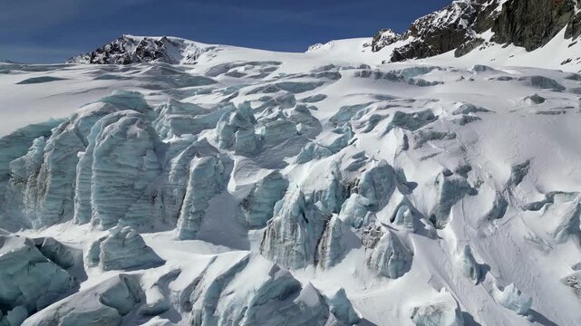 Aerial view of the Schonbielhutte SAC area with its rugged glacier, deep snow crevasses, and towering mountain peaks under a clear blue sky in Zermatt, Wallis, Switzerland.