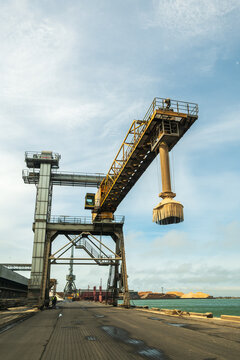 View of the industrial crane at the Port of Ventspils with piles of wood chips in the background under a blue sky in Ventspils, Ventspils Municipalit, Latvia.
