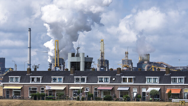 View of the Tata Steel industrial plant rising behind a row of traditional residential houses in Velsen-Noord, Noord-Holland, Netherlands.