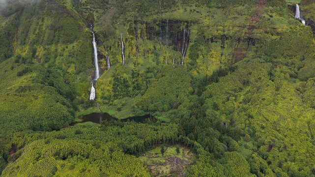 Aerial view of the lush green cliffs and multiple waterfalls of Poco da Ribeira do Ferreiro in Fajazinha, Azores, Portugal.