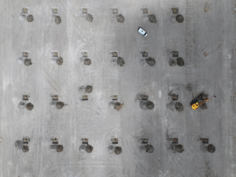 Aerial view of a construction site featuring a grid of foundation piles, an excavator, and a vehicle on a grey ground surface in Netherlands.