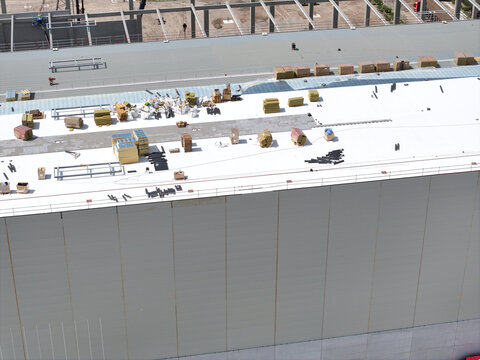 Aerial view of a large industrial building roof under construction, featuring scattered building materials, insulation panels, and structural steel beams in the Netherlands.