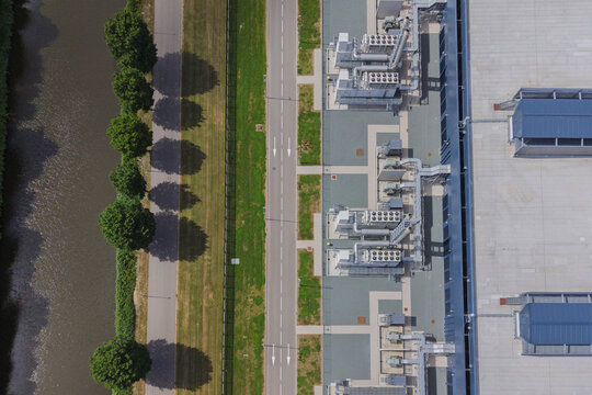 Aerial view of a modern data center facility with cooling units, adjacent to a road, a row of trees, and a canal in Middenmeer, North Holland, Netherlands.