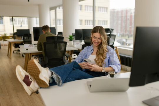 Woman relaxing at office desk looking at smartphone during break