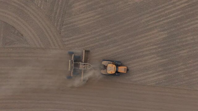 Aerial view of a yellow tractor pulling agricultural equipment across a dusty field in Middenmeer, North Holland, Netherlands.