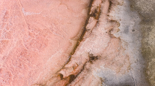 Aerial view of pastel pink salt deposits blending into weathered mineral textures with layered organic patterns and soft earthy tones, France.