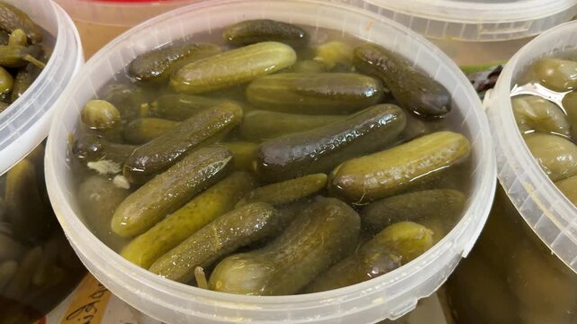 Fresh market pickles in container, closeup of clear plastic tub packed with brined cucumbers, glistening brine