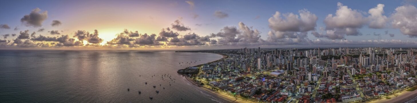 Aerial view of the coastal city of Joao Pessoa with its skyline, sandy beaches, and the Atlantic Ocean under a dramatic sunset sky in Joao Pessoa, Paraiba, Brazil.
