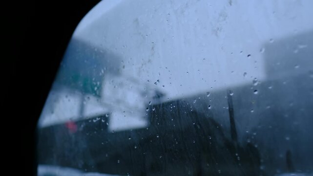 raindrops and condensation on a fogged car window with blurred buildings visible through the wet glass. Cool blue tones, soft focus, and natural rainy light create a dramatic atmospheric background