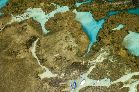 Aerial view of Piscinas naturais em Ponta do Seixas with vibrant coral reefs, turquoise water, small boats, and people swimming in Joao Pessoa, State of Paraiba, Brazil.