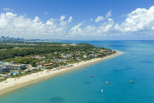 Aerial view of Seixas Beach with turquoise water, sandy coastline, coastal vegetation, and distant city skyline in Joao Pessoa, Paraiba, Brazil.