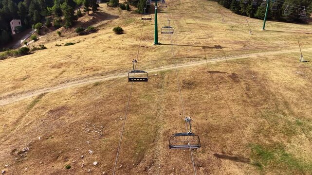 Aerial top-down view of an idle chairlift line running over sun-dried brown grass on a ski slope at La Molina resort, Catalan Pyrenees, Spain, during the summer off-season