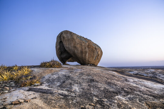 View of Lajedo de Pai Mateus, a massive granite boulder formation on a rocky landscape with sparse vegetation under a clear sky in Cabaceiras, Paraiba, Brazil.