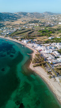 Aerial view of the coastline with turquoise waters, sandy beach, and white buildings in Paros, Greece.