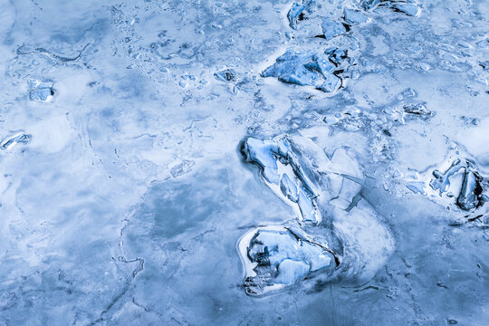 Aerial view of ice fragments floating on the frozen surface of Fjallsarlon glacier lagoon with deep blue textures and cracked ice patterns in Sveitarfelagid Hornafjordur, Iceland.