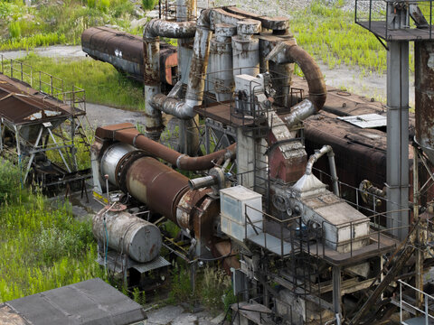 Aerial view of rusted industrial machinery and metal pipes at an abandoned factory site surrounded by overgrown vegetation in Krakow, Lesser Poland Voivode, Poland.