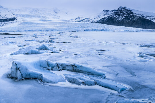 Aerial view of the frozen Fjallsarlon glacier lagoon with scattered icebergs and snow-covered mountains in the background in Sveitarfelagid Hornafjordur, Iceland.