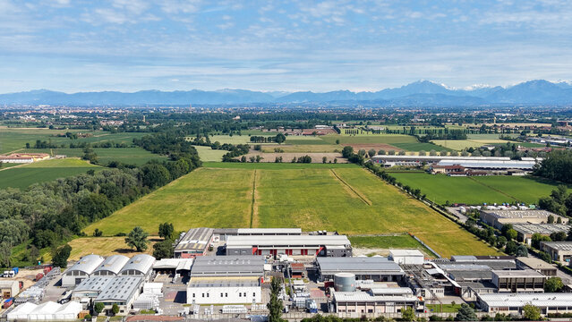 Aerial view of an industrial zone bordered by agricultural fields with the Alps rising in the background in Caleppio, Lombardy, Italy.
