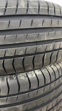 Stacked summer tires at dealership close-up showing clear tread patterns and rubber texture, passenger car sizes arranged in neat