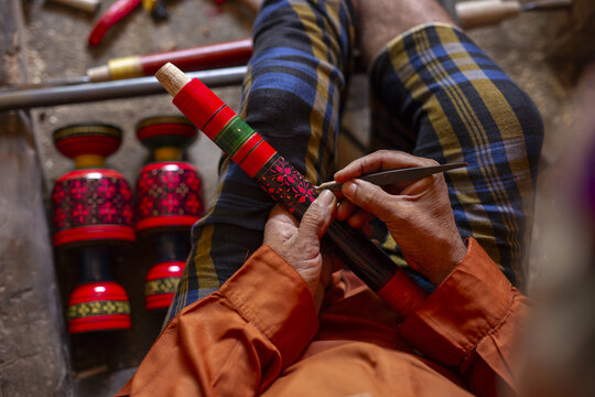 View of a craftsman meticulously carving intricate floral patterns into a traditional lacquered wooden piece with vibrant red, green, and black colors in Kashmore, Sindh, Pakistan.