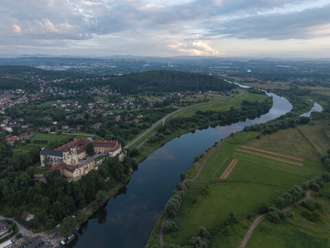 Aerial view of the Benedictine Abbey in Tyniec perched on a cliff above the Vistula River, surrounded by green fields, forests, and the suburban landscape of Krakow, Lesser Poland, Poland.